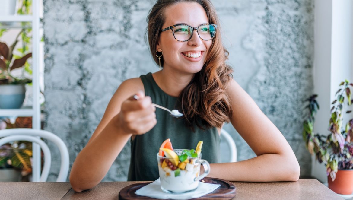Recenzja e-booka wydanego przez NFZ dla chorych na zespół jelita nadwrażliwego (IBS). Uśmiechnięta kobieta w okularach je zdrowy deser w kawiarni.