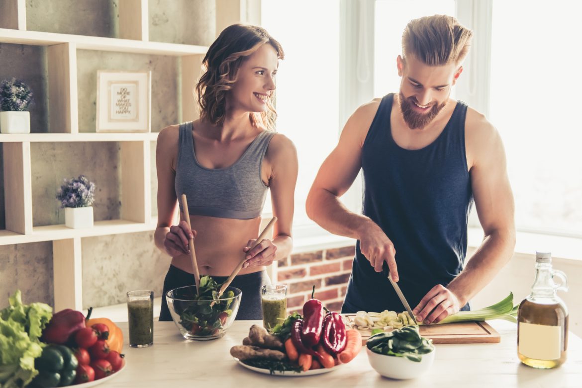 Posiłek przed treningiem i posiłek potreningowy - jak powinny wyglądać? Kobieta i mężczyzna przygotowują jedzenie w kuchni po treningu.