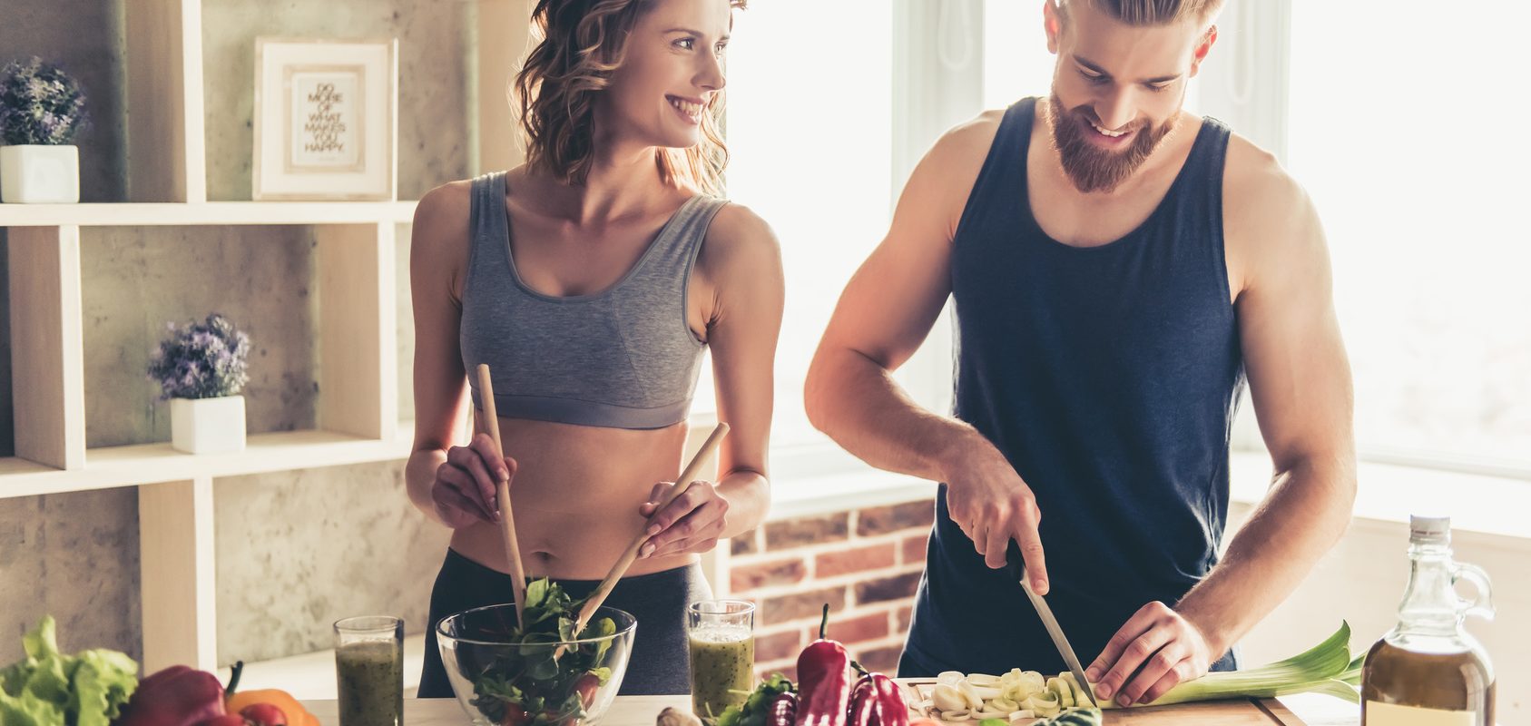 Posiłek przed treningiem i posiłek potreningowy - jak powinny wyglądać? Kobieta i mężczyzna przygotowują jedzenie w kuchni po treningu.