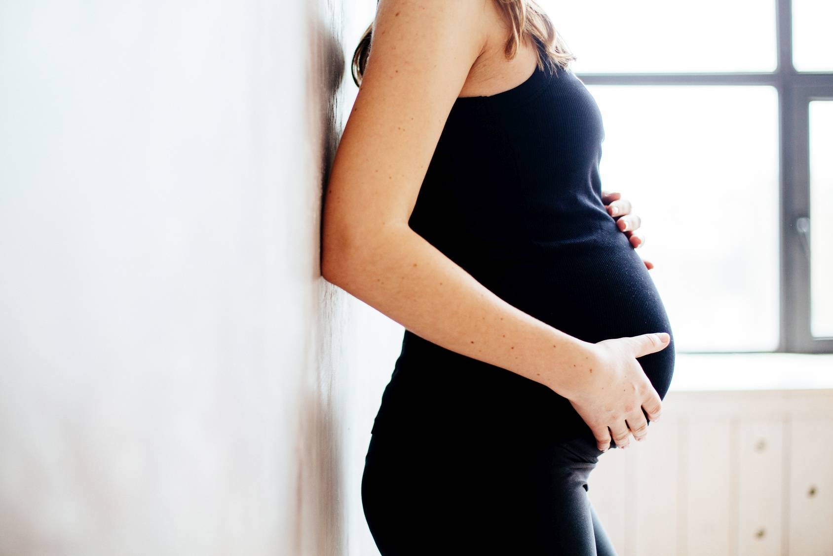 Jaki powinien być poziom TSH w ciąży? Kobieta w czarnym stroju sportowym dotyka brzucha w zaawansowanej ciąży.