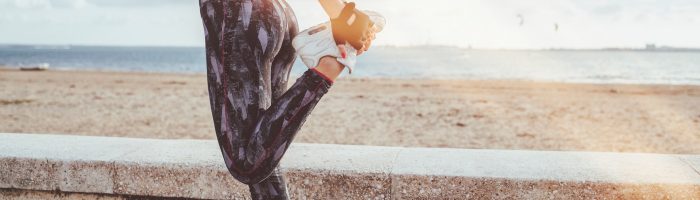 Jak powinna wyglądać rozgrzewka przed treningiem? Kobieta w sportowym stroju przygotowuje się do biegania na świeżym powietrzu.