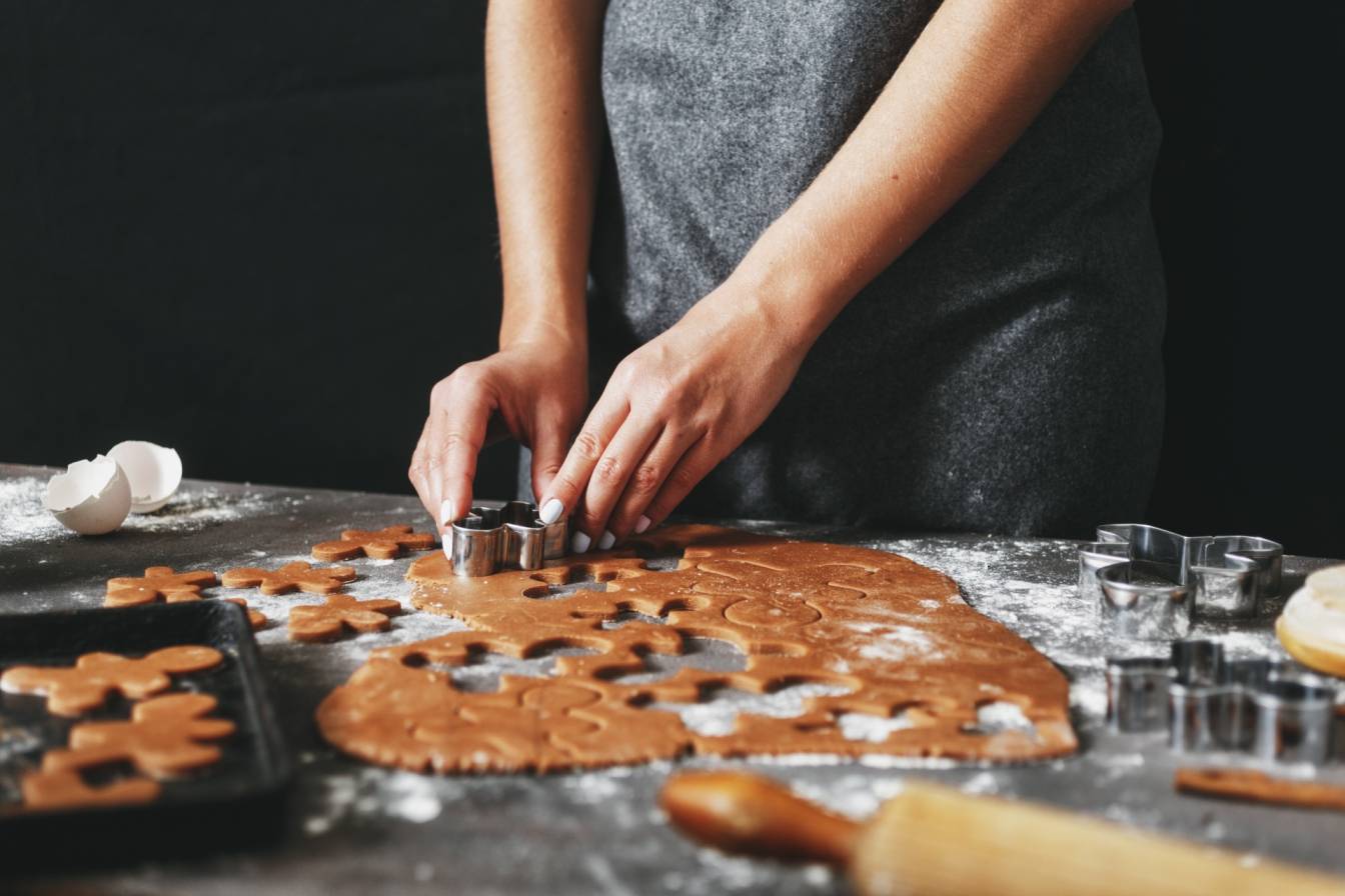 Przepis na pierniczki świąteczne - jak je przygotować i dlaczego warto wyrabiać ciasto ręcznie? Kobieta wycina świąteczne pierniczki z rozwałkowanego ciasta.