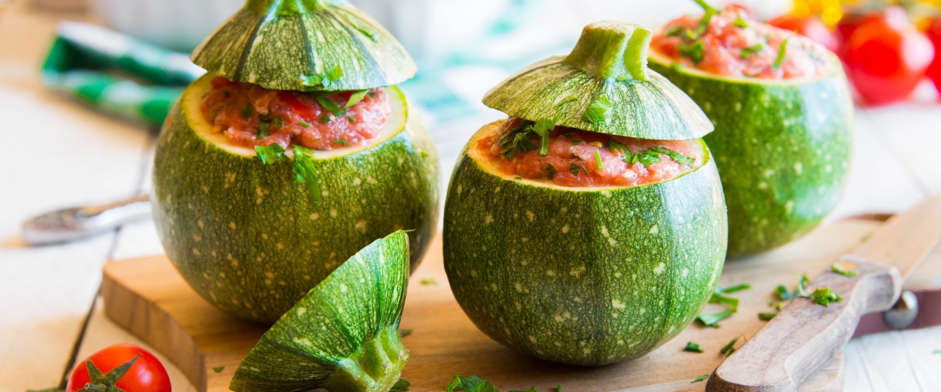 Dania z cukinii. Okrągłe cukinie faszerowane mięsem i warzywami na drewnianej desce do krojenia i jasnym blacie.