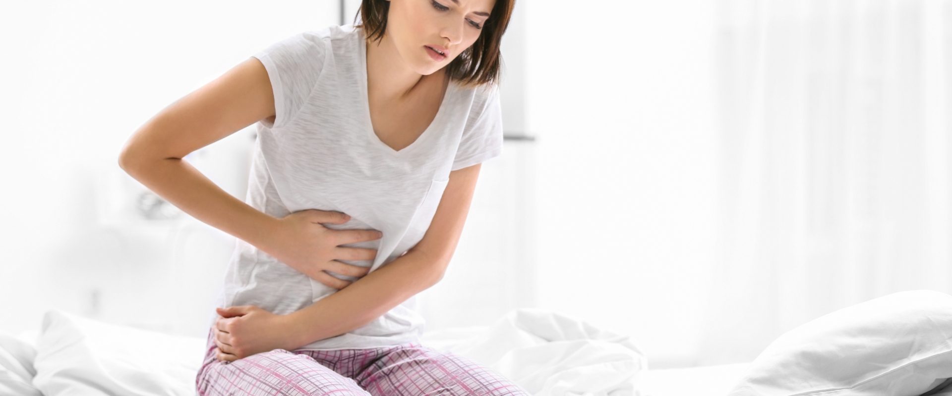 Przepuklina brzuszna - przyczyny, objawy, leczenie. Kobieta siedzi w piżamie na łóżku i trzyma się za bolący brzuch.