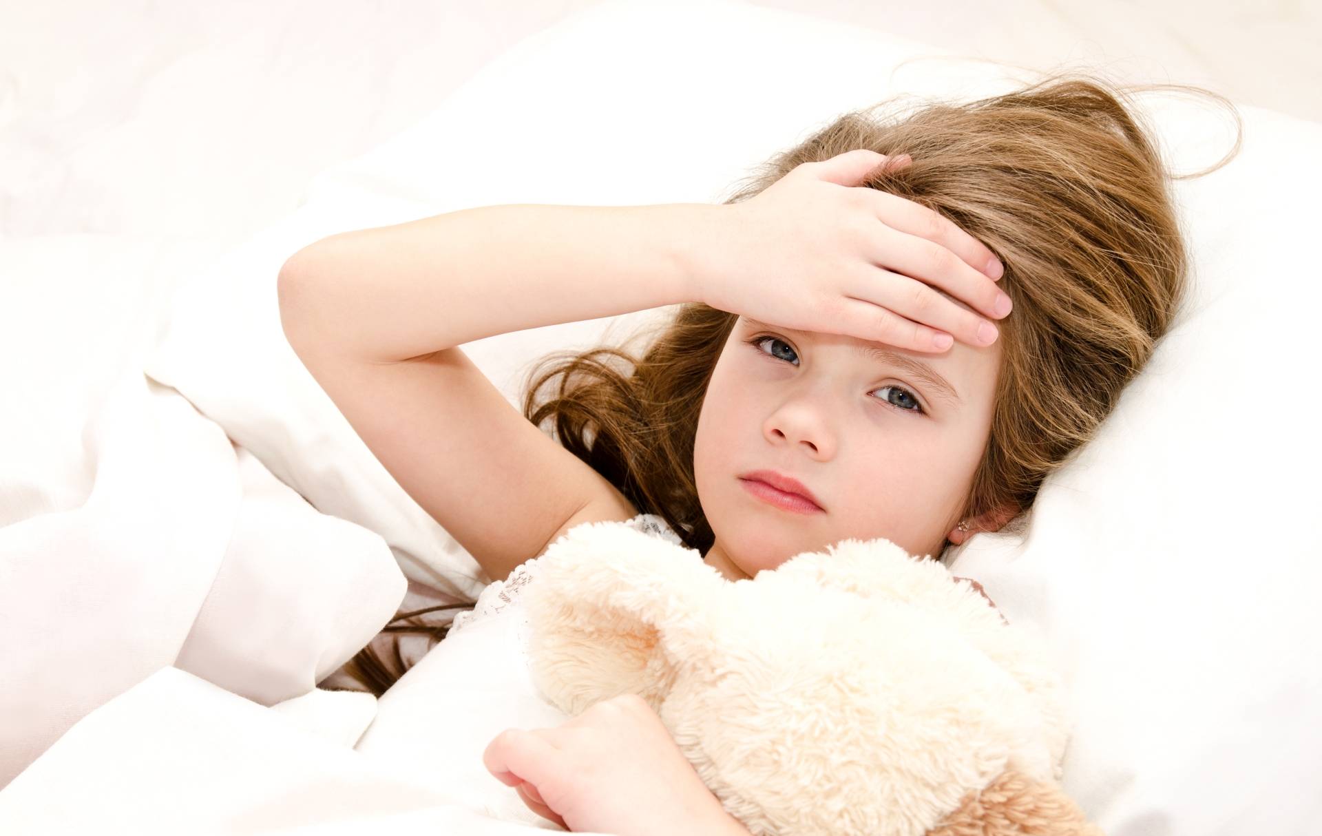 Dziewczynka z gorączką leży w łóżku i przytula misia. Sposoby na przeziębienie u dzieci.