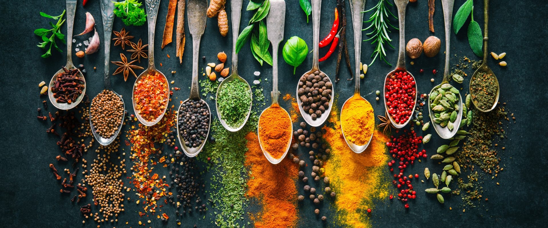Jak gotować jesienią według medycyny chińskiej? Rozgrzewające przyprawy i zioła na ułożonych obok siebie łyżeczkach i czarnym tle.