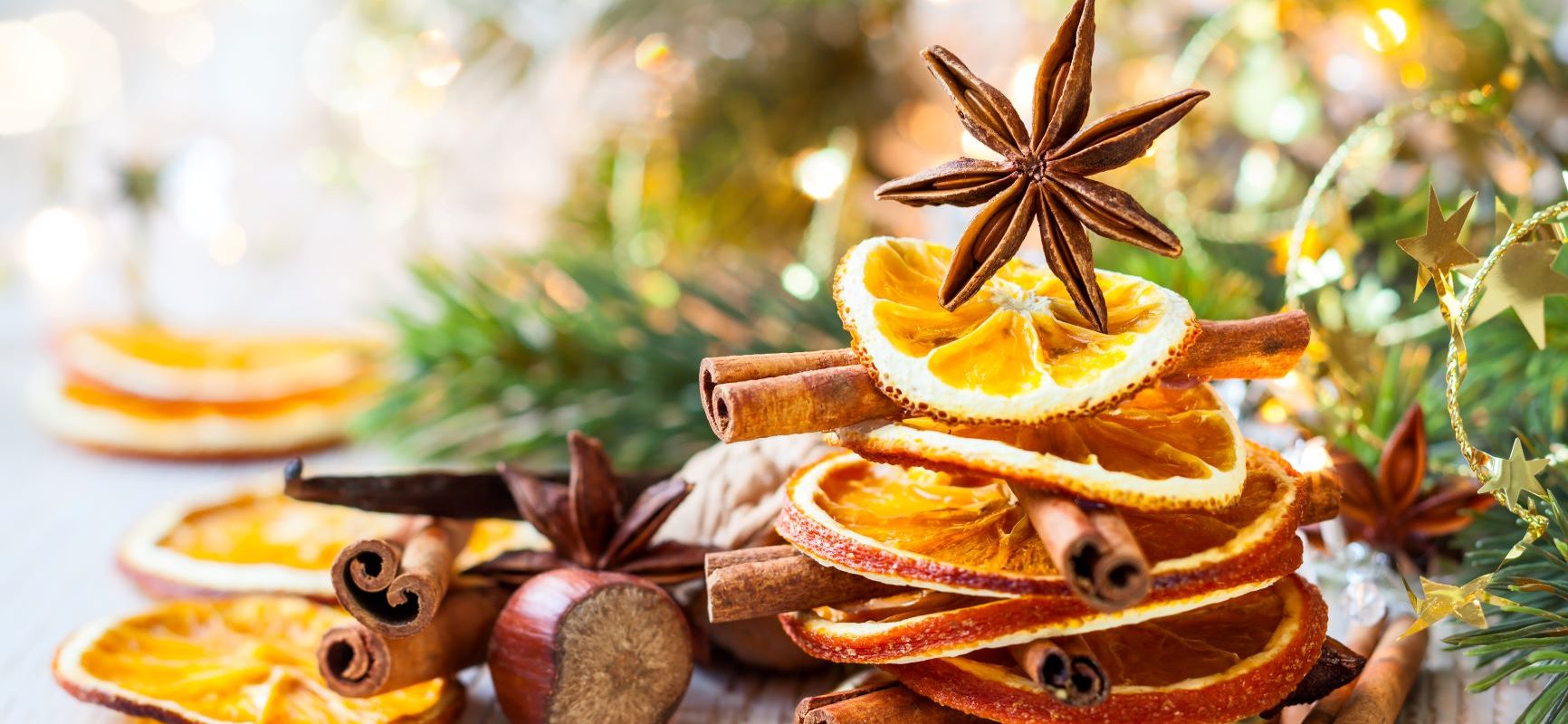 Świąteczne przyprawy na Wigilię i Boże Narodzenie. Cynamon, goździki, kardamon, gałka muszkatołowa, imbir. Suszone plastry cytrusów i laski cynamonu ułożone na kształt choinki, anyż na górze jako gwiazda, wokół leżą przyprawy.