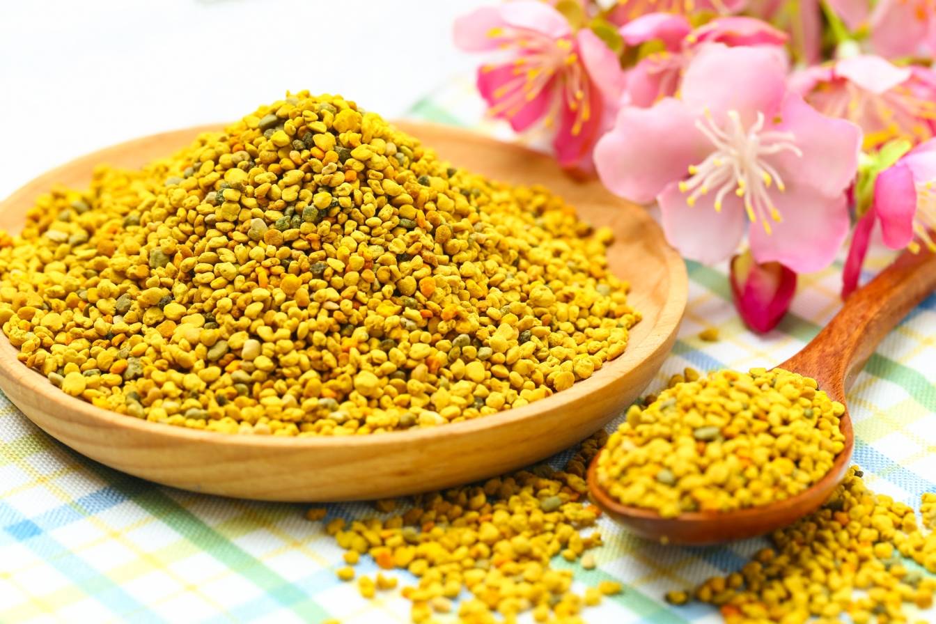 Pyłek pszczeli na drewnianym talerzu i łyżce na stole powleczonym ceratą kratkę. Jak stosować pyłek i jakie ma działanie?