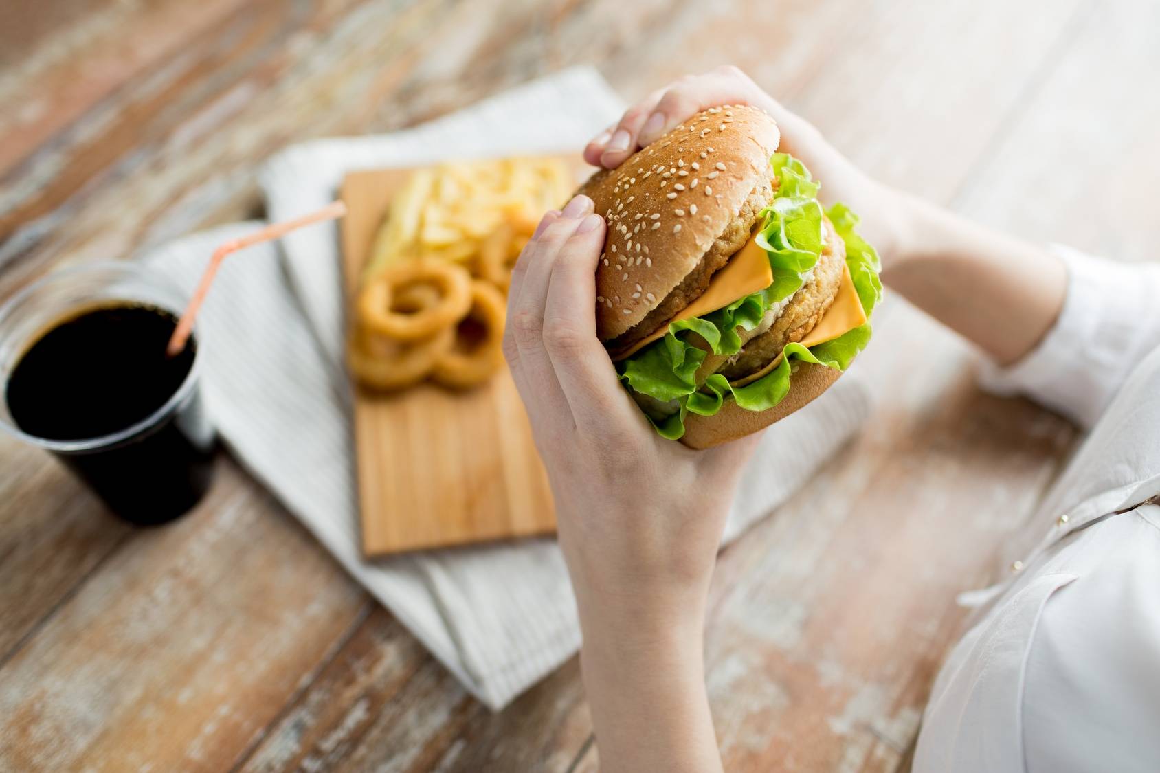 Zła dieta przy refluksie i zgadze: fast-food, słodycze i słone przekąski. Zbliżenie na hamburgera w kobiecych dłoniach.