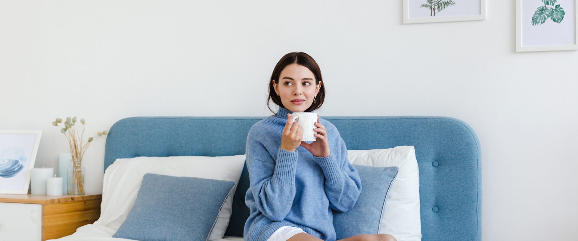 Jakie czynniki obniżają odporność? Kobieta w niebieskim swetrze siedzi na łóżku i pije gorącą herbatę.