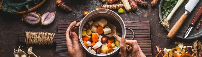 Retrowarzywa, o których warto sobie przypomnieć. Odkryj 7 najlepszych retrowarzyw i sprawdź przepisy. Widok z góry na kobiece ręce w kuchni, przygotowujące potrawkę z warzyw korzeniowych.