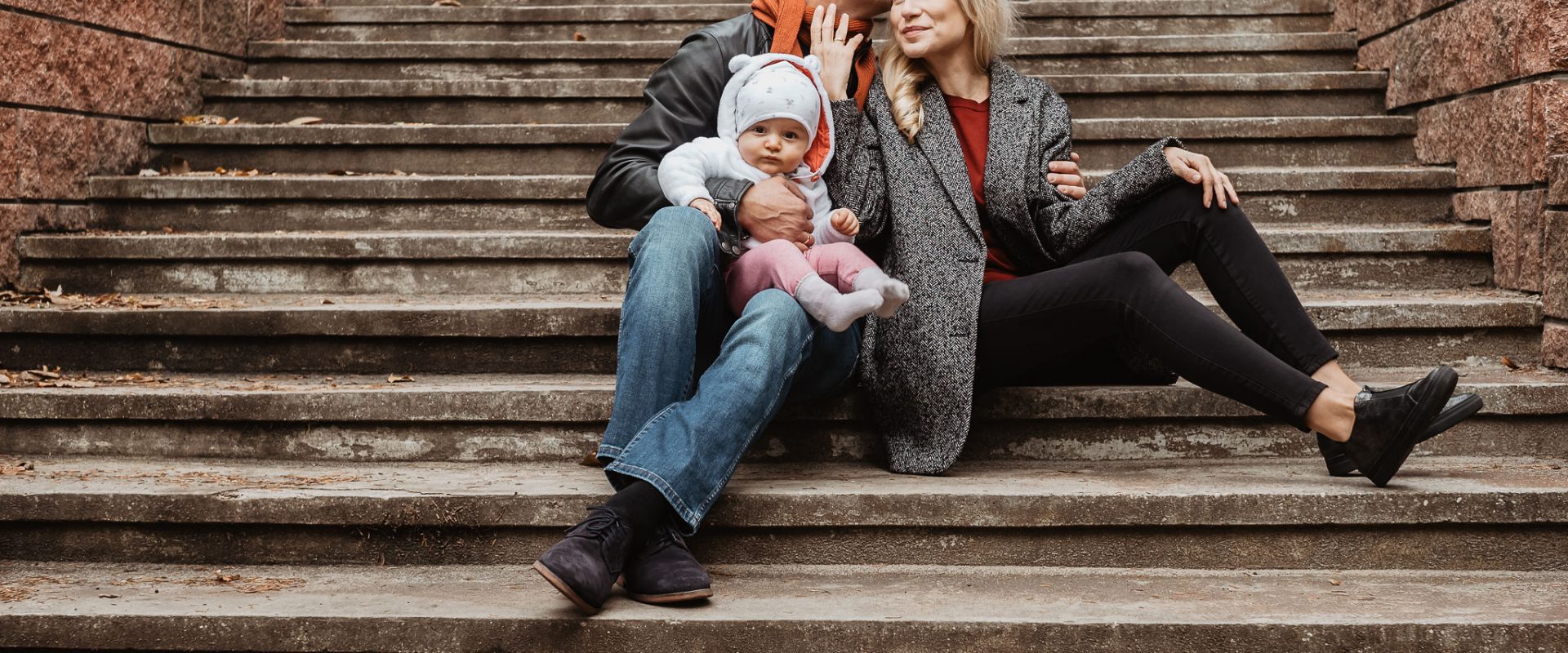 Monika Sobień-Górska i Robert Górski z córką siedzą przytuleni na schodkach.