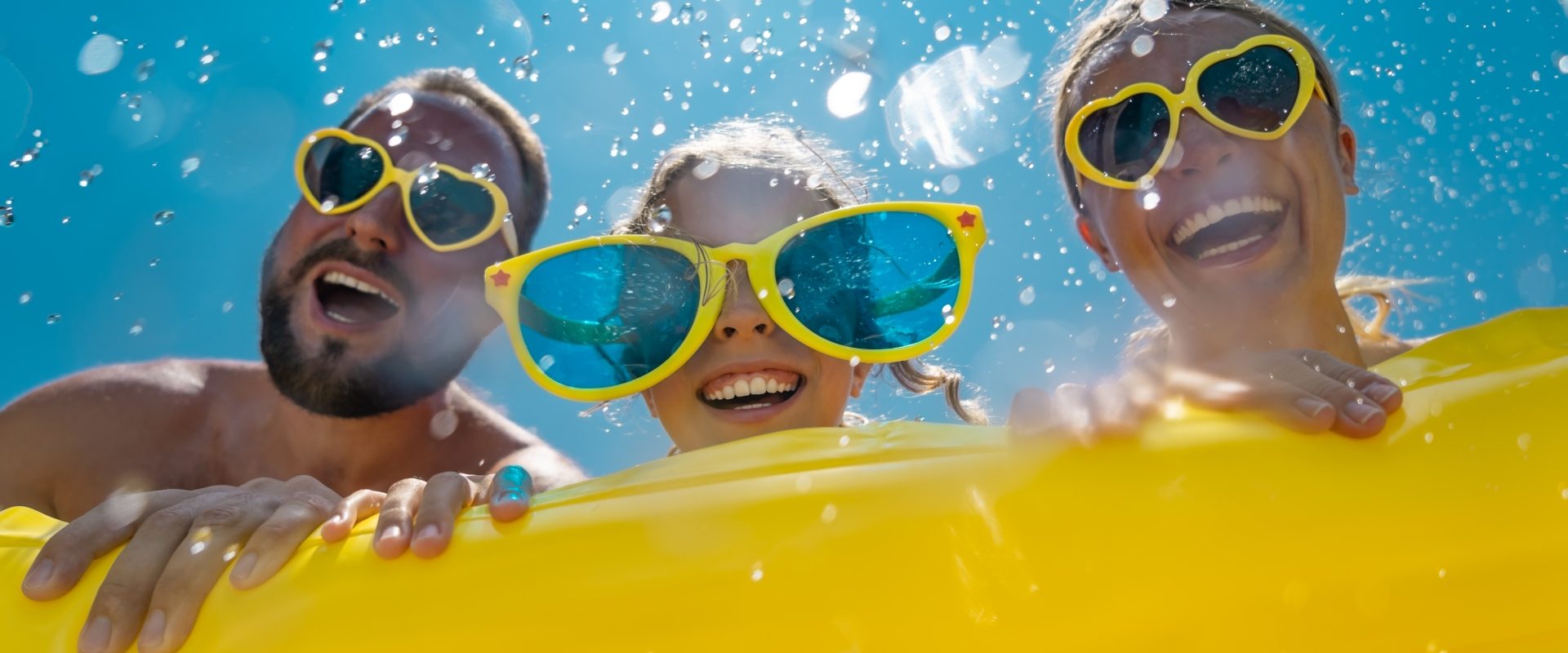 Jak zadbać o oczy latem? Opowiada prof. Jerzy Szaflik. Szczęśliwa rodzina w żółtych okularach na wakacjach spędza czas w basenie.
