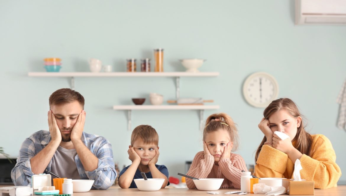 Rośliny i zioła przeciwwirusowe - poznaj 5 najskuteczniejszych. Przeziębiona rodzina - mama, tata, córka, syn - siedzą przy stole przy śniadaniu i smarczą w chusteczki do nosa.