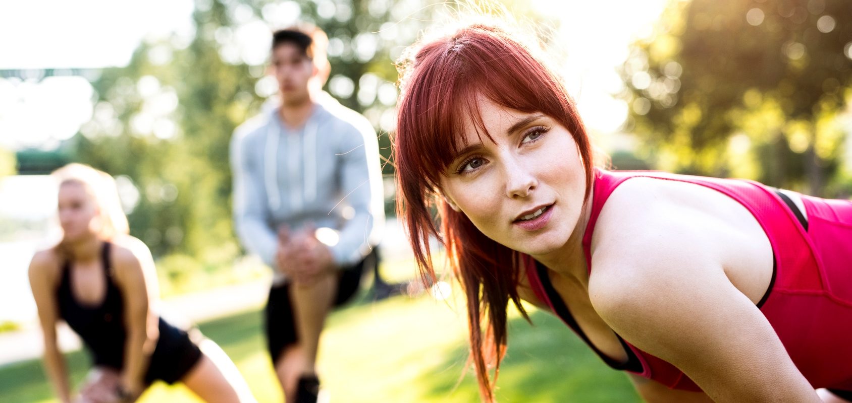 Naturalne sposoby na ból stawów. Trójka przyjaciół rozgrzewa się przed treningiem w parku.