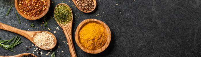 Przyprawy rozgrzewające - kolorowe mielone przyprawy na drewnianych łyżkach na czarnym blacie kuchennym.