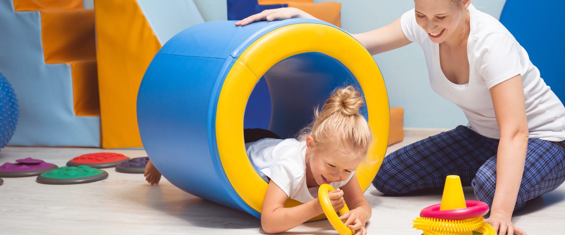 Integracja sensoryczna (SI) u dzieci. Dziewczynka wykonuje ćwiczenia pod okiem instruktorki na zajęciach z integracji sensorycznej.