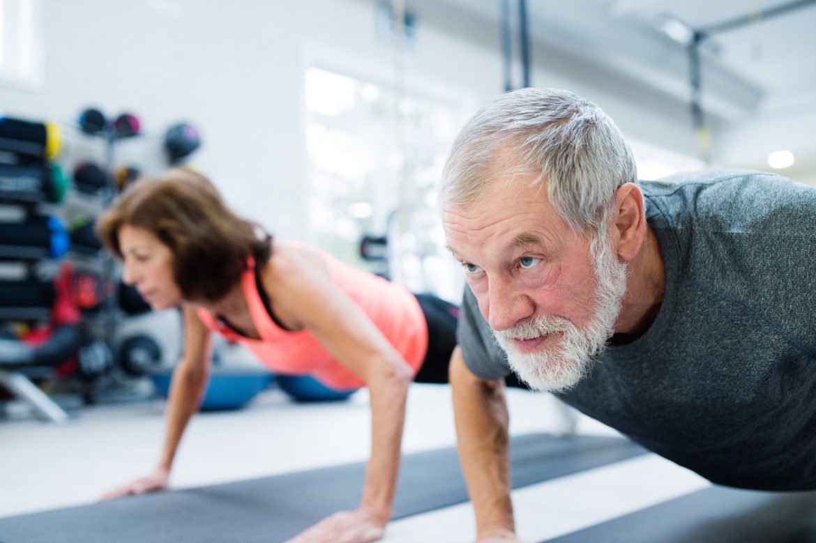 Siłownia dla seniora - jakie ćwiczenia dla seniorów będą najlepsze? Starszy mężczyzna i kobieta ćwiczą na macie na siłowni.