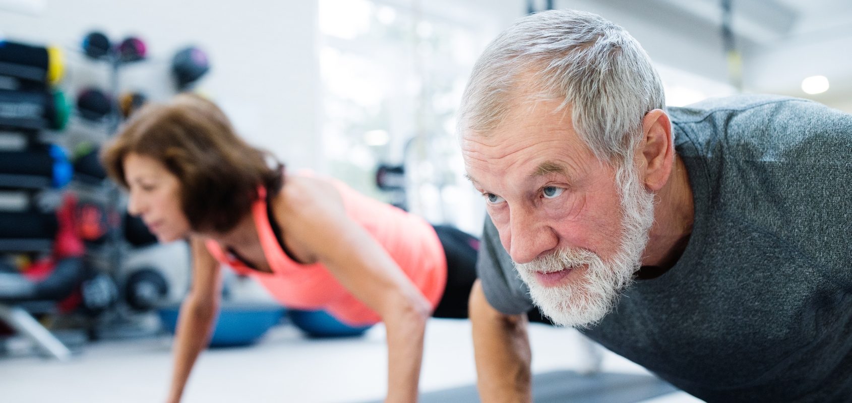 Siłownia dla seniora - jakie ćwiczenia dla seniorów będą najlepsze? Starszy mężczyzna i kobieta ćwiczą na macie na siłowni.