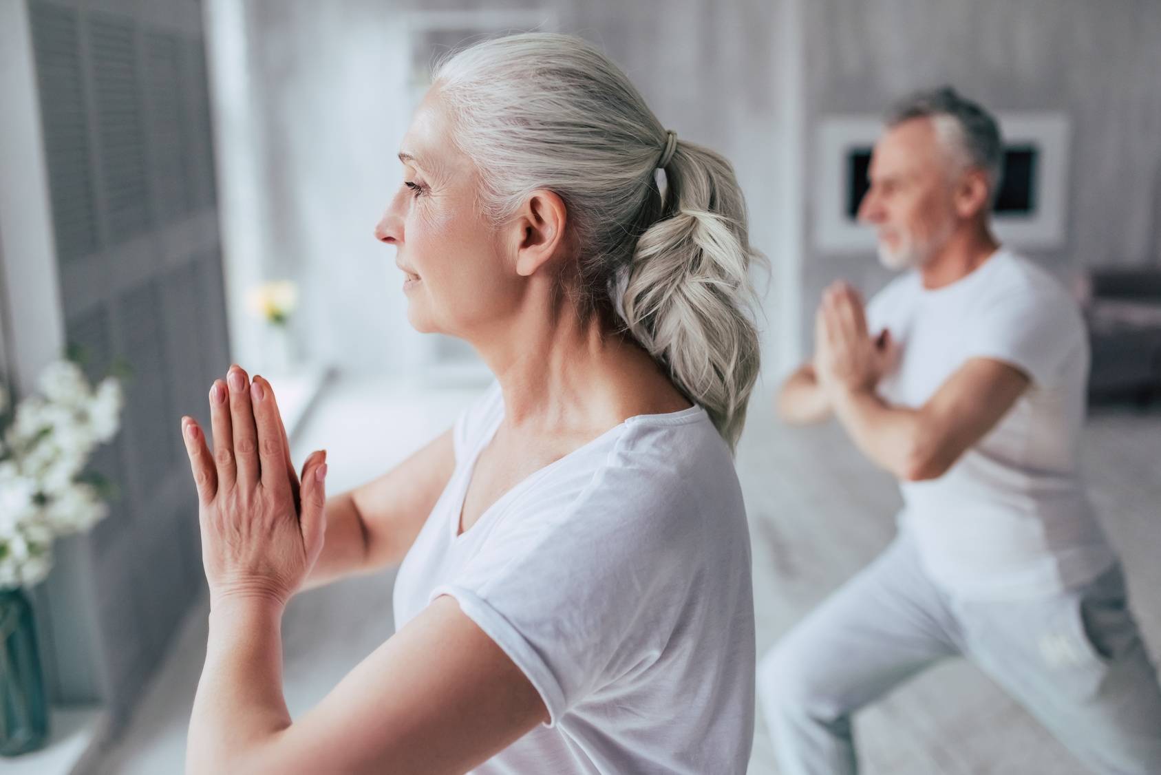 Joga i rozciąganie wspierają pracę powięzi. Para seniorów w szarych dresach ćwiczy jogę lub tai chi.