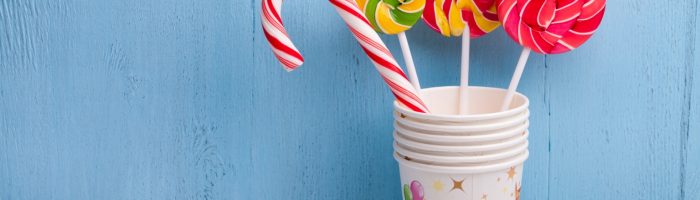 Cukrzyca typu 2 - jakie są jej przyczyny i jak ją leczyć. Na niebieskim tle w nałożonych na siebie papierowych kubeczkach stoją 4 kolorowe lizaki.