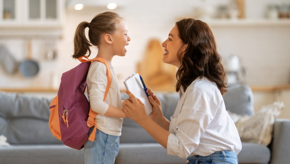 Jak budować poczucie własnej wartości u dzieci? Słowa, które pomogą wzmocnić poczucie własnej wartości u dziecka. Mama rozmawia z córką w salonie przed wyjściem do szkoły.