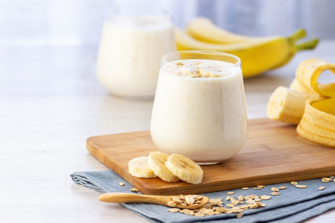 Banan - wartości odżywcze i właściwości. Ile kalorii ma banan? Co zrobić z bananów? Smoothie z banana w szklance na drewnianej deseczce w kuchni.
