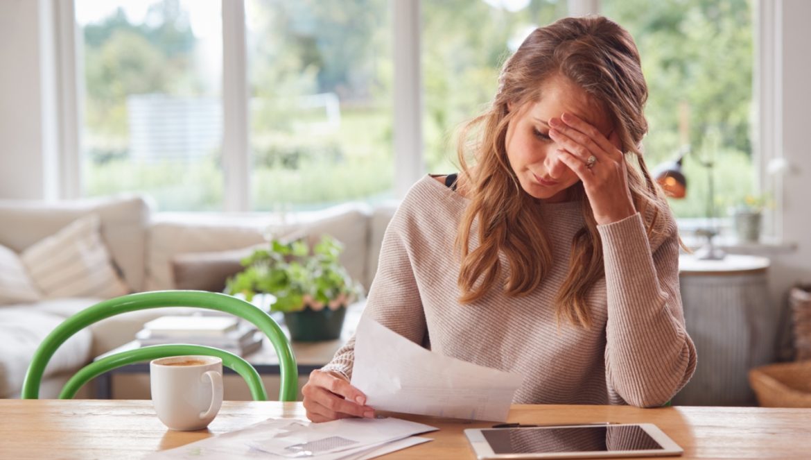 Endometrioza - przyczyny, objawy i leczenie. Jak żyć z endometriozą? Załamana kobieta siedzi przy stole w domu nad dokumentami.