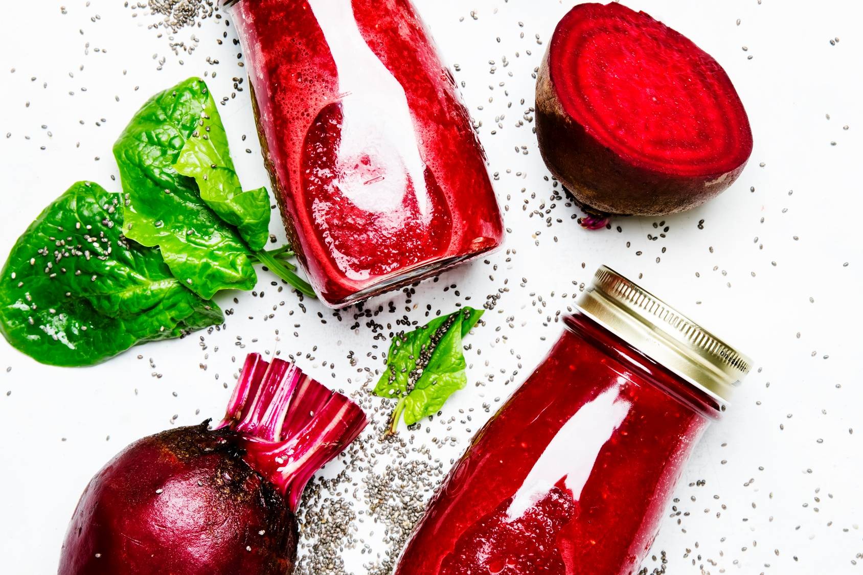 Zakwas buraczany. Domowe sposoby na alergię: probiotyki na alergię. Na białym tle leżą szklane butelki z sokiem z buraków, przekrojone surowe buraki i liście.