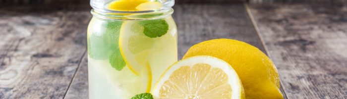 Przepis na domowy izotonik. Słoik z lemoniadą cytrynową i miętą stoi na ciemnej drewnianej powierzchni, obok leży przekrojona cytryna.