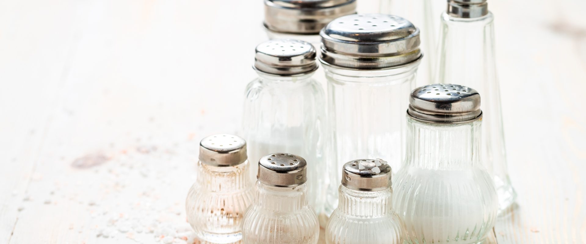 Natrium muriaticum - lek homeopatyczny. Kilka solniczek ustawionych na rustykalnym blacie, obok leży rozsypana sól.