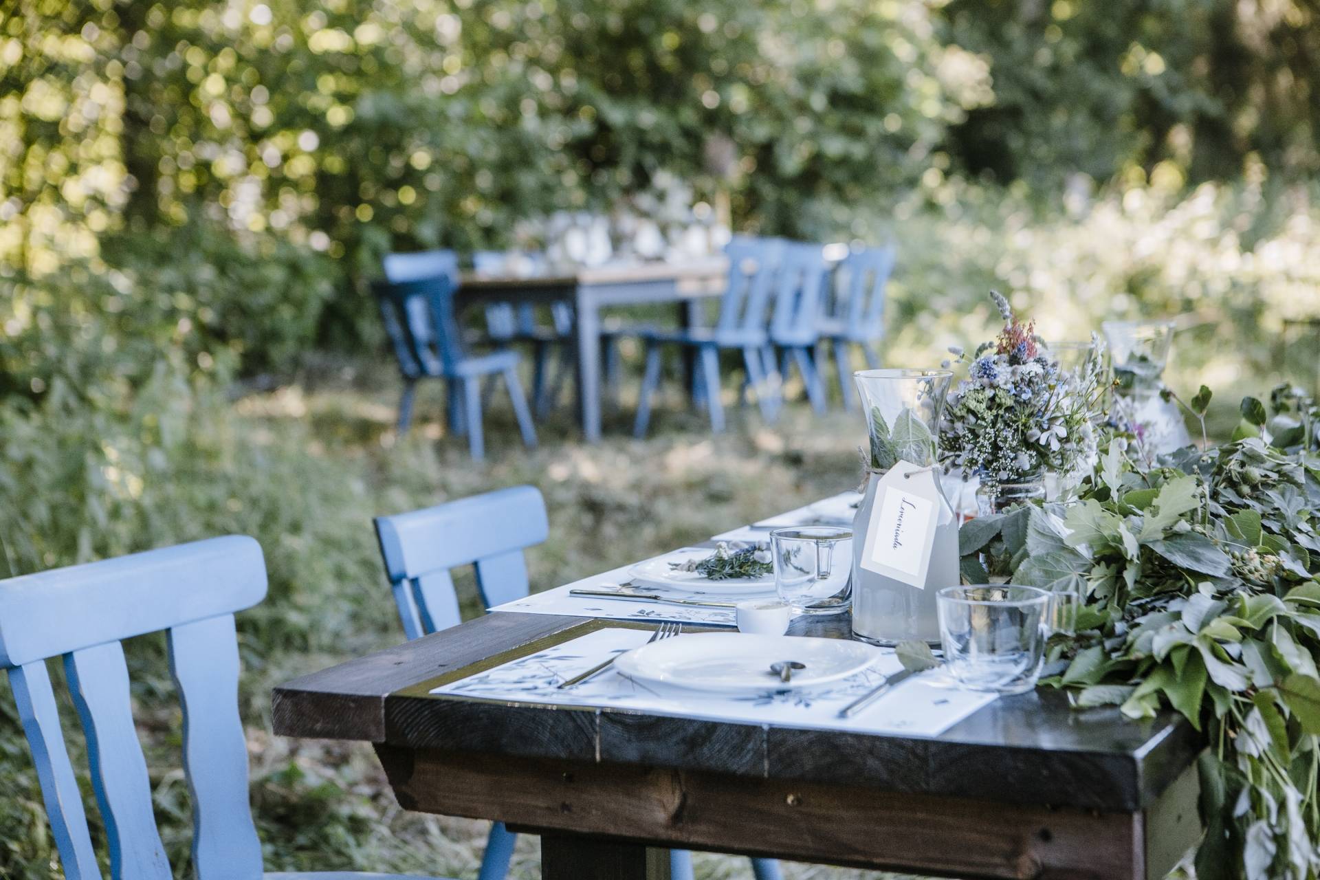 Leśne uczty na Mazurach - projekt LAS RAZ Agnieszki Żelazko. Stoły i krzesła drewniane stoją w środku lasu.