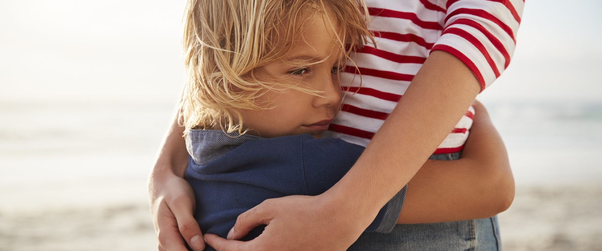 Stres u dzieci - objawy. Chłopiec przytula się do mamy na plaży.