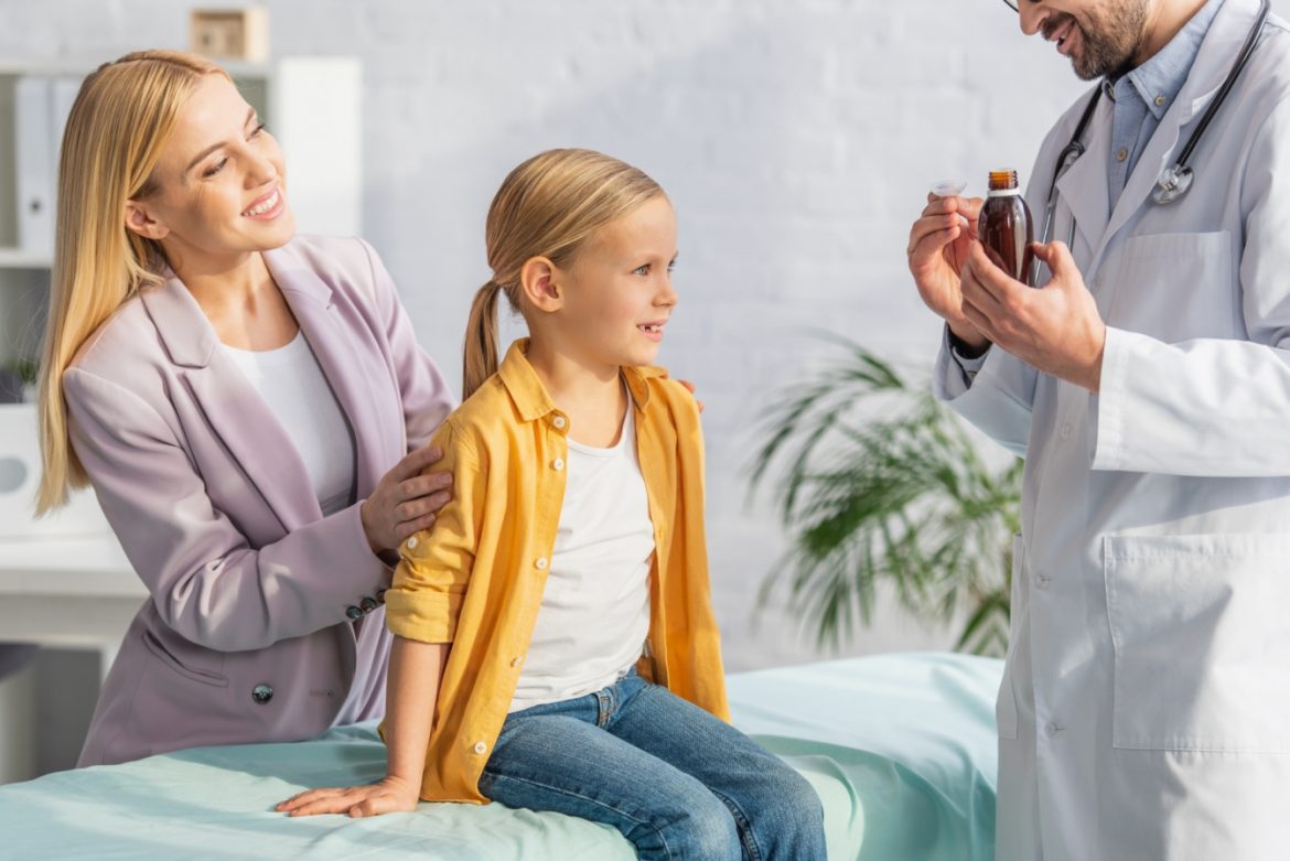 Jak wybrać najlepszy syrop dla dziecka na odporność? Lekarz pokazuje mamie i jej córce syrop na odporność.