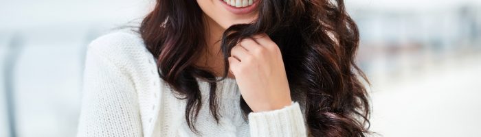 5 sposobów na przesilenie wiosenne. Kobieta o długich ciemnych włosach w białym swetrze uśmiecha się do aparatu.
