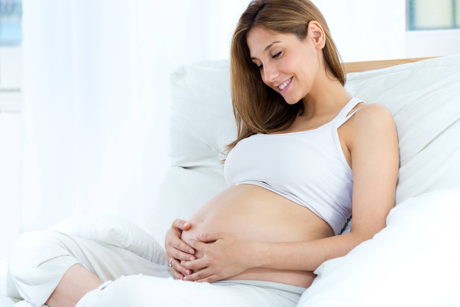 Dlaczego poród boli? Kobieta w ciąży siedzi na łóżku i dotyka swojego brzucha.