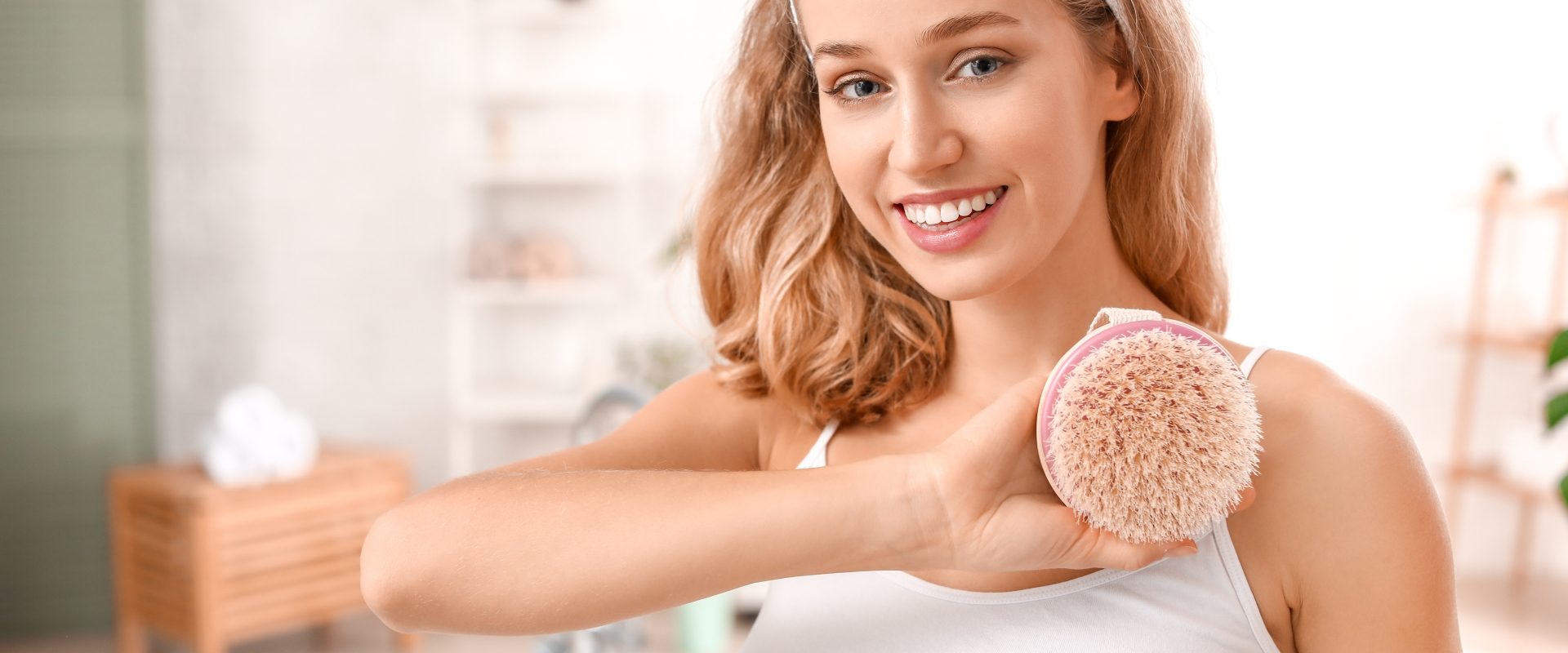 Szczotkowanie ciała na sucho - jak ujędrnić skórę? Młoda kobieta trzyma szczotkę do ciała w łazience.