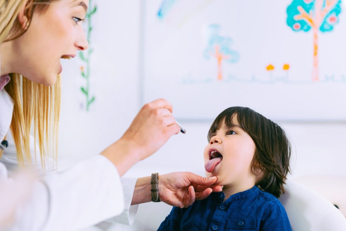 Szkarlatyna (płonica) - objawy, przyczyny i leczenie. Pediatra bada małego pacjenta, sprawdzając czy ma zaczerwienione gardło.