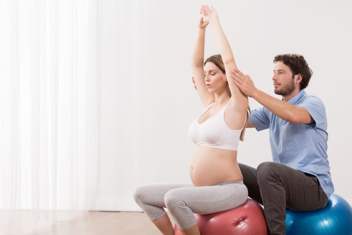 Szkoła rodzenia - co warto o niej wiedzieć? Jak przygotować się do porodu? Kobieta w ciąży ćwiczy na piłce z partnerem.