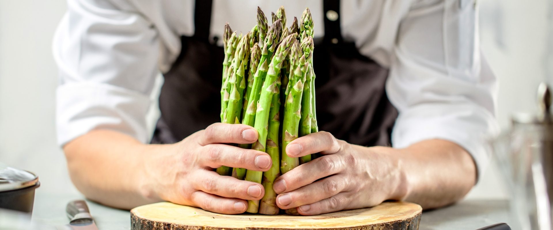 Przepisy na szparagi. Szef kuchni trzyma pęczek szparagów tuż przed pokrojeniem ich na desce.