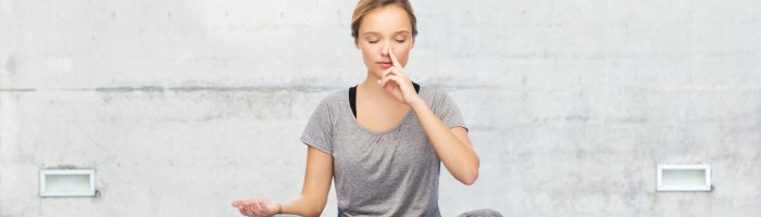 Sztuka oddechu w praktyce jogi. Kobieta w szarym stroju sportowym ćwiczy pranajamę ma macie - oddech w jodze.