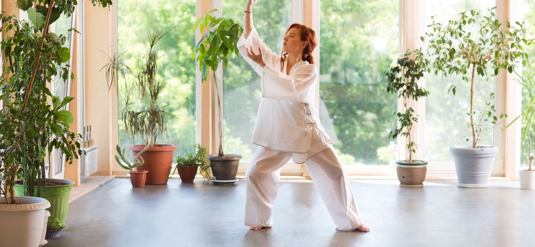 Tai chi - medytacja w ruchu. Kobieta praktykuje tai chi w domu w otoczeniu roślin.