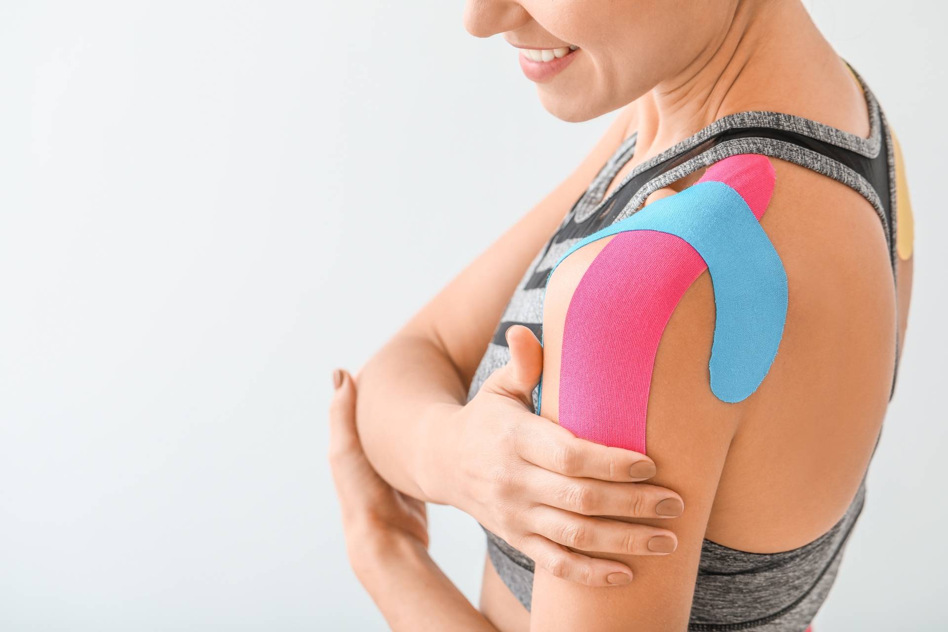 Kinesiotaping - co to jest? Kobieta w stroju sportowym ma przyklejone tejpy na bark.