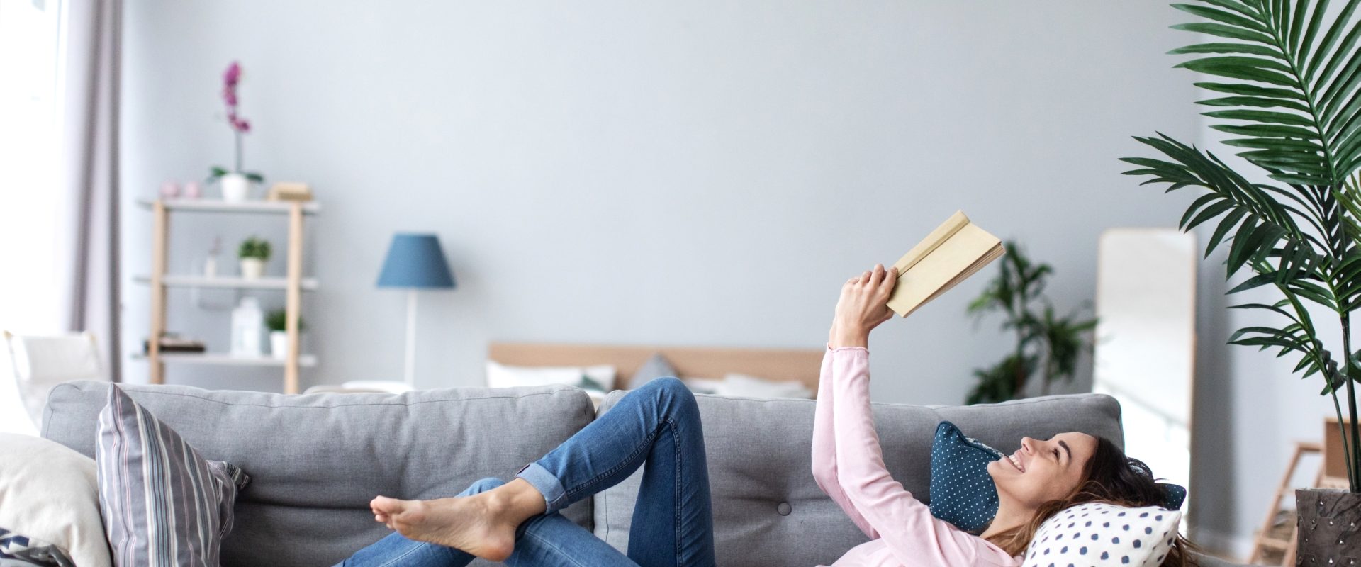 Trening umysłu - na czym polega? Jak ćwiczyć mózg? Dziewczyna leży na kanapie w salonie i czyta książkę.