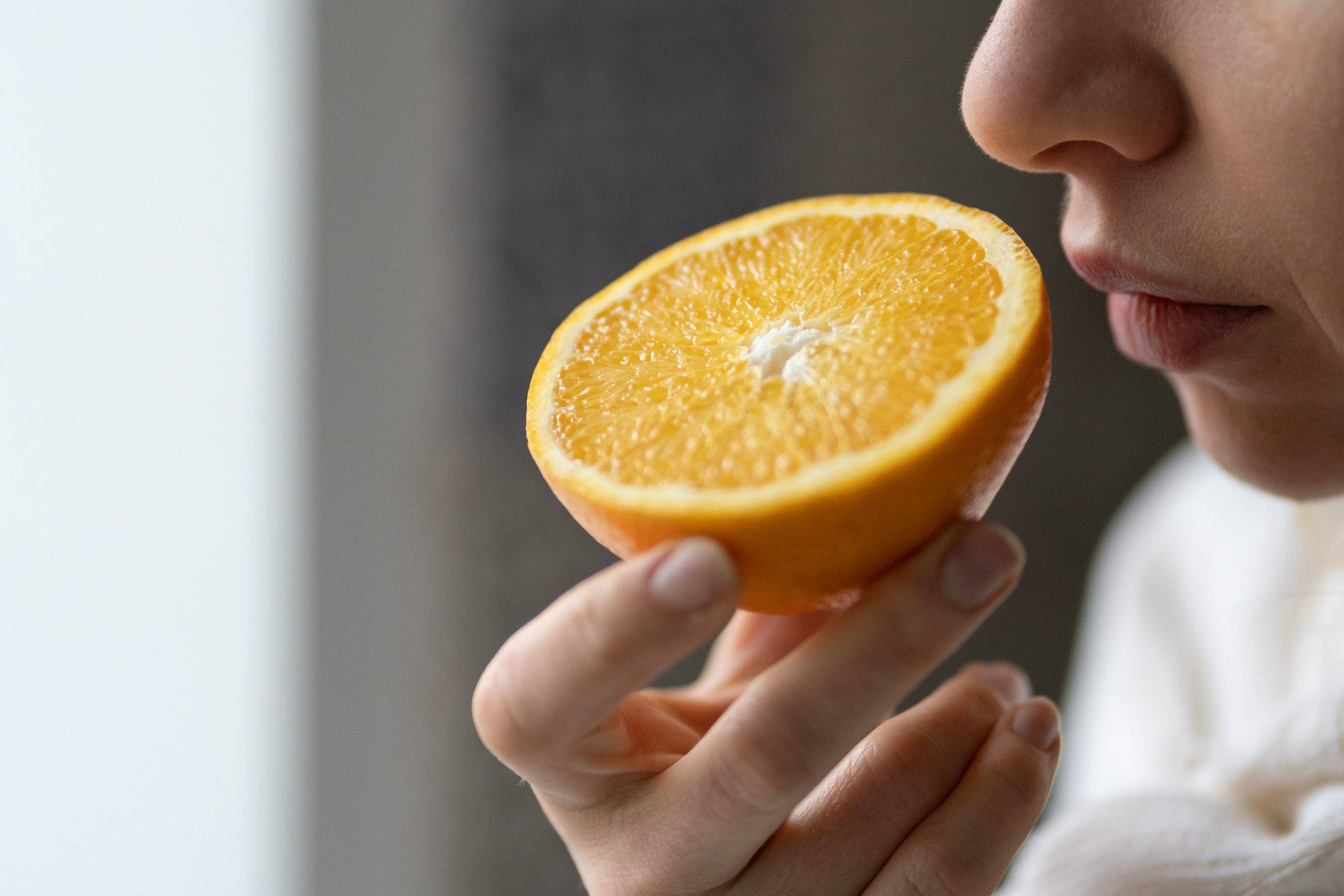 Trening węchowy - jak go stosować po przejściu choroby COVID-19? Kobieta wącha przekrojoną połówkę pomarańczy.