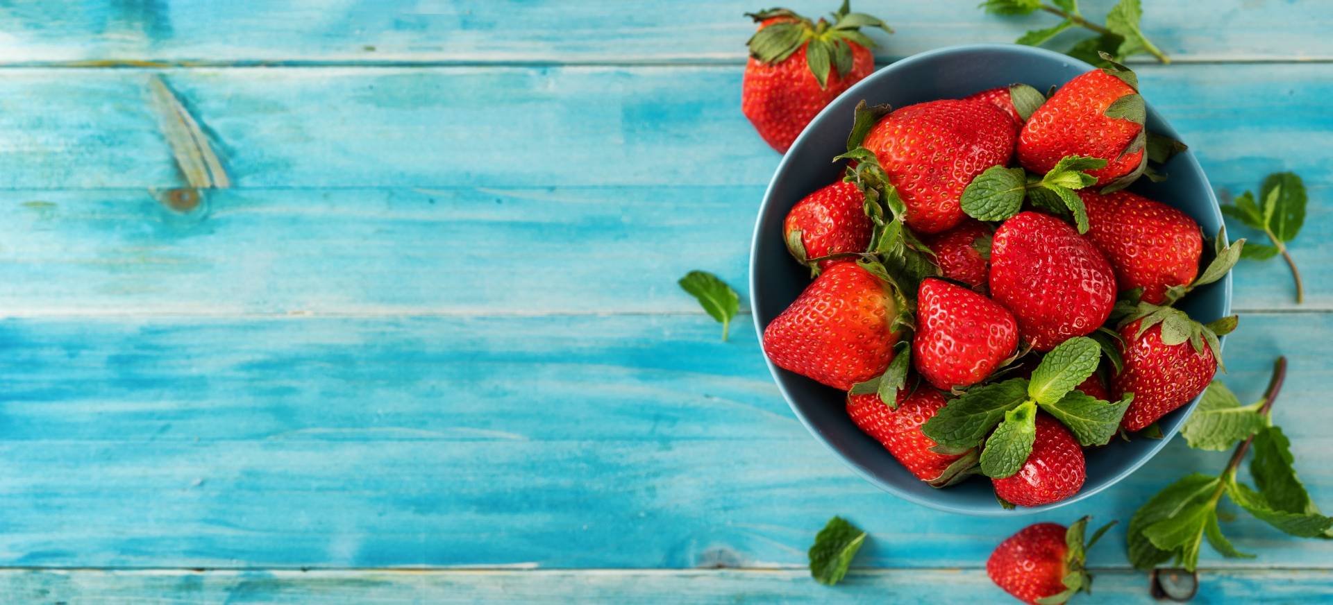 Truskawki w niebieskiej misce na niebieskim drewnianym blacie.