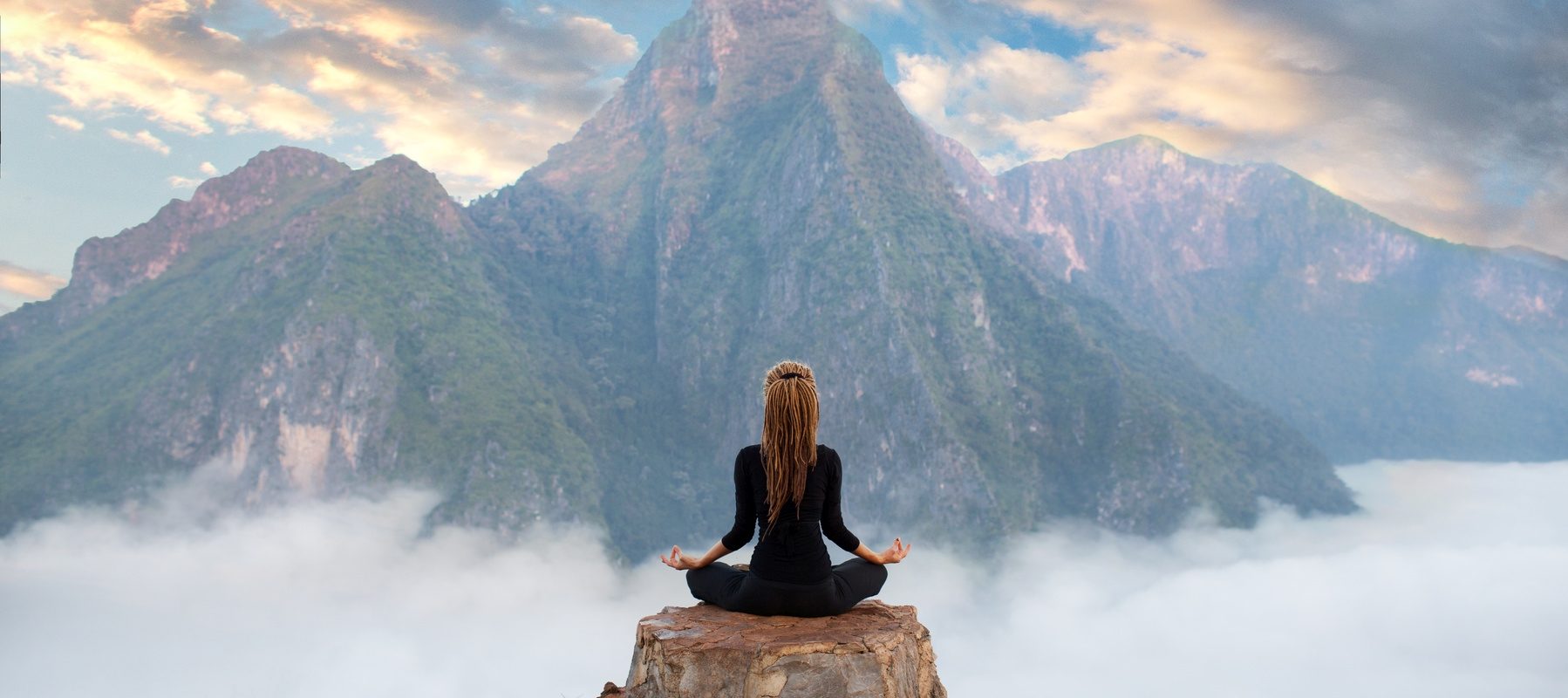 Rytuały tybetańskie, które warto wcielić w życie. Kobieta medytuje siedząc na skale ponad chmurami w Tybecie.