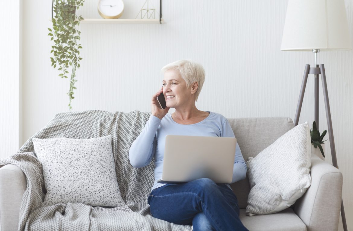 Silicea - lek homeopatyczny z krzemionki. Seniorka siedzi na kanapie z laptopem na kolanach i rozmawia przez komórkę.