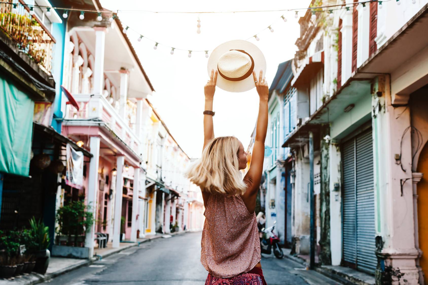 Witamina D pomaga schudnąć. Szczupła opalona blondynka spaceruje uliczkami Hawany i unosi w dłoniach ciały kapelusz chroniący przed słońcem.