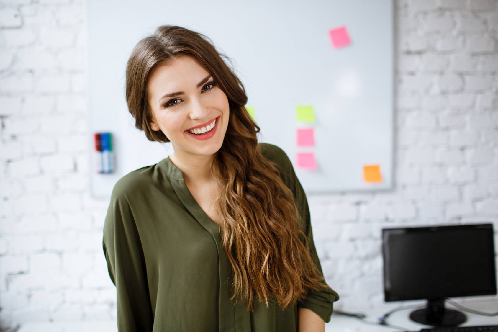 Koło życia - jak zrobić bilans, który pomoże podsumować dotychczasowy etap życia i dokonać zmian na lepsze. Uśmiechnięta kobieta w biurze na tle tablicy z karteczkami post-it.